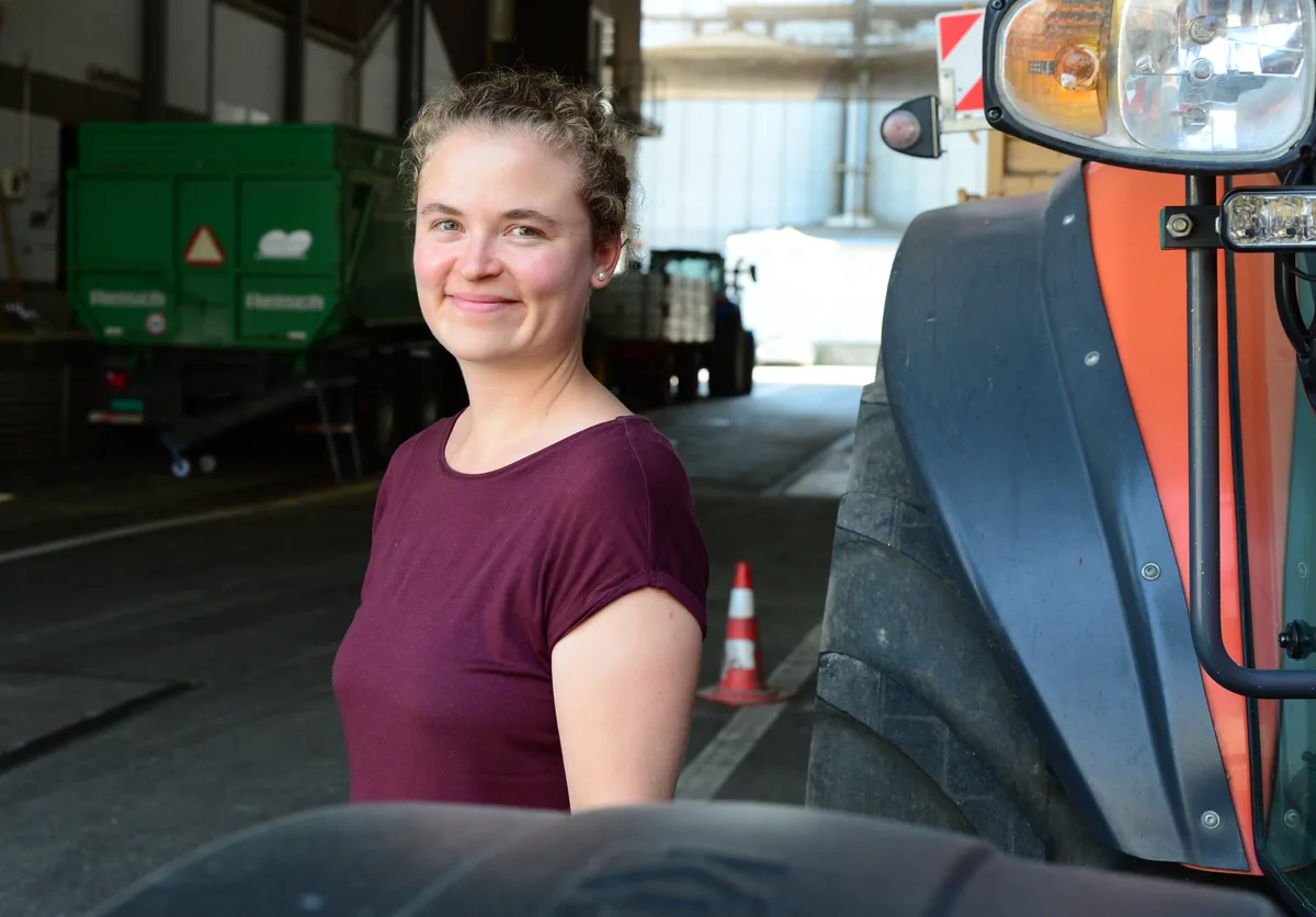 Eine junge Frau steht in einer Halle neben einem Traktor.
